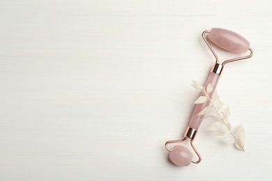 Photo of Natural rose quartz face roller and leaves on white wooden background, flat lay. Space for text