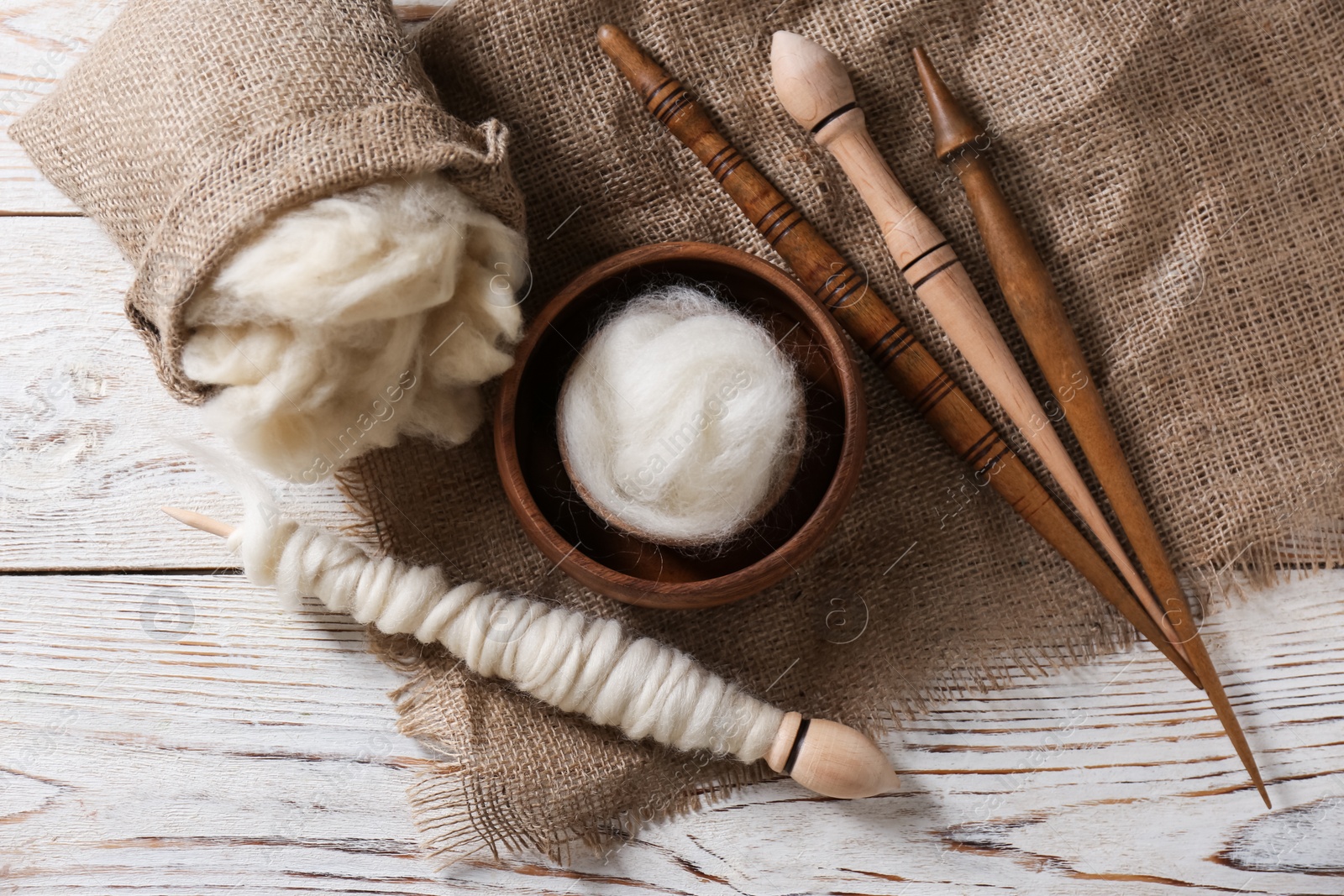 Photo of Soft wool and spindles on white wooden table, flat lay