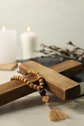 Wooden cross, rosary beads, Bible and church candles on white table, closeup