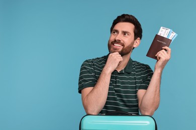 Smiling man with passport, suitcase and tickets on light blue background. Space for text
