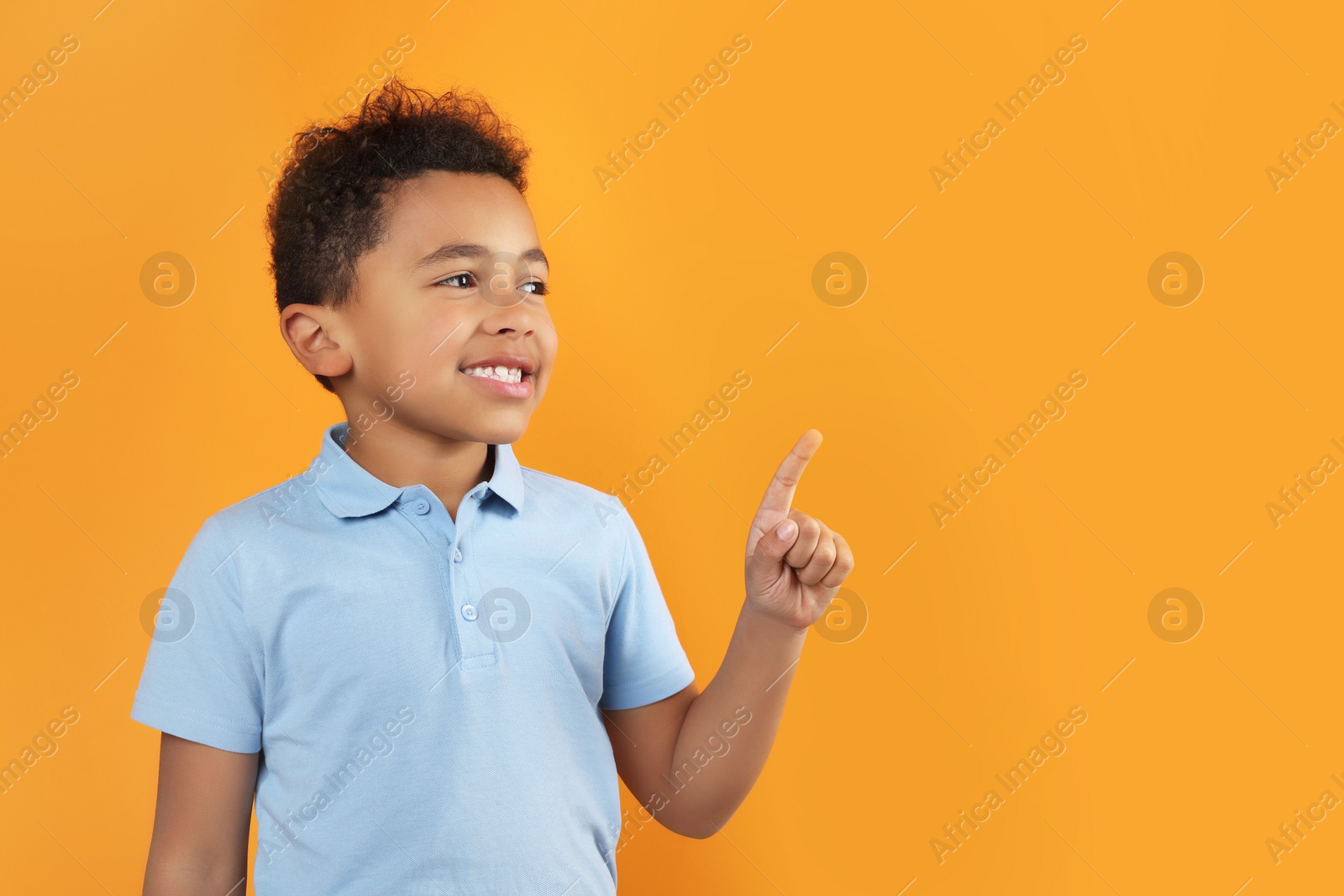 Photo of Cute African-American boy pointing on orange background. Space for text