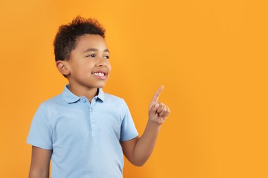 Cute African-American boy pointing on orange background. Space for text