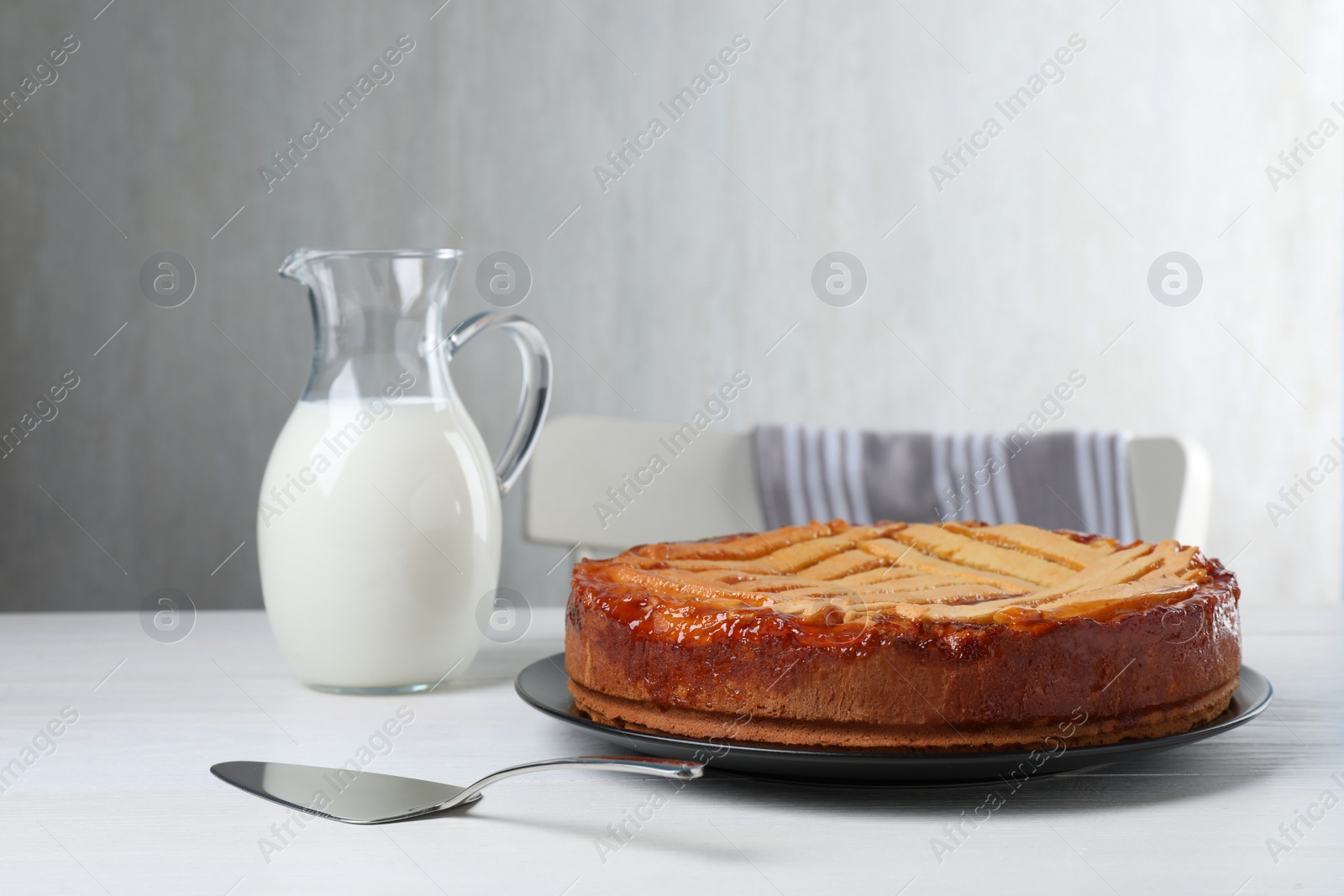 Photo of Tasty apricot pie and jug of milk on white wooden table