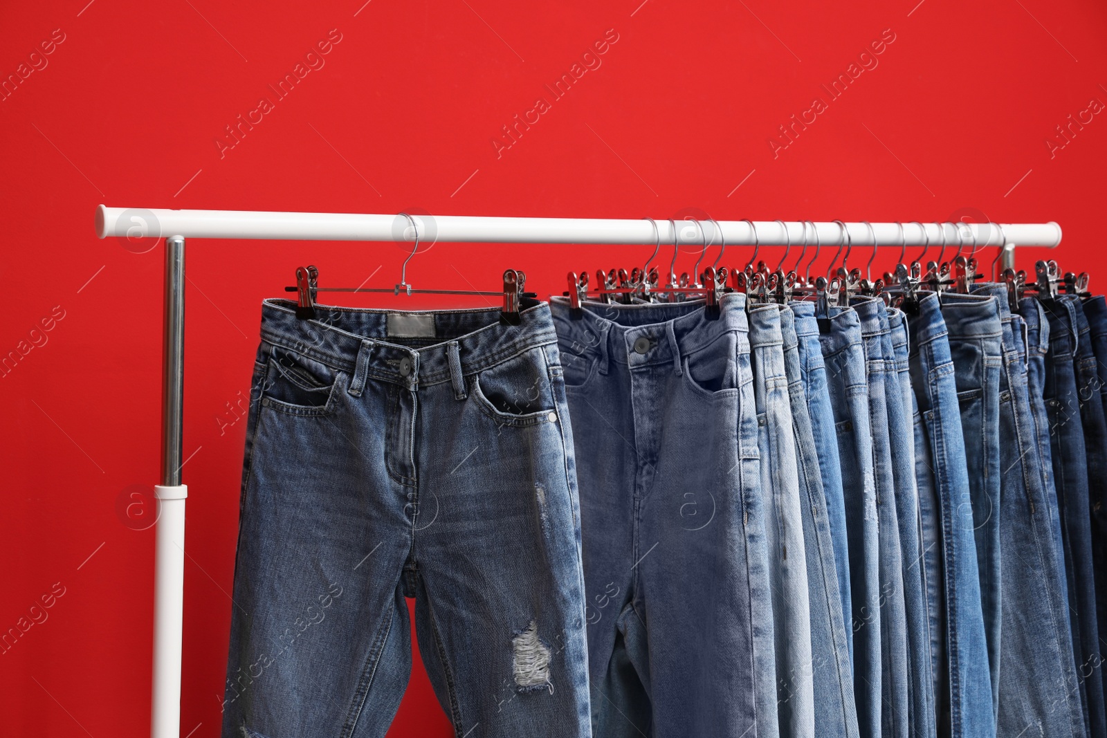 Photo of Rack with stylish jeans on red background, closeup