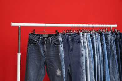 Photo of Rack with stylish jeans on red background, closeup