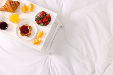 Photo of Tray with delicious breakfast on bed, top view. Space for text