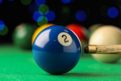 Photo of Billiard ball with number 2 and cue on green table, closeup