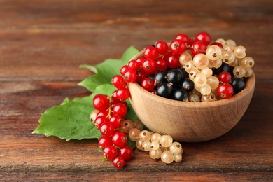 Photo of Different fresh ripe currants and green leaves on wooden table, closeup. Space for text