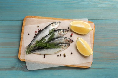 Fresh raw sprats, cut lemon, dill and peppercorns on light blue wooden table, top view