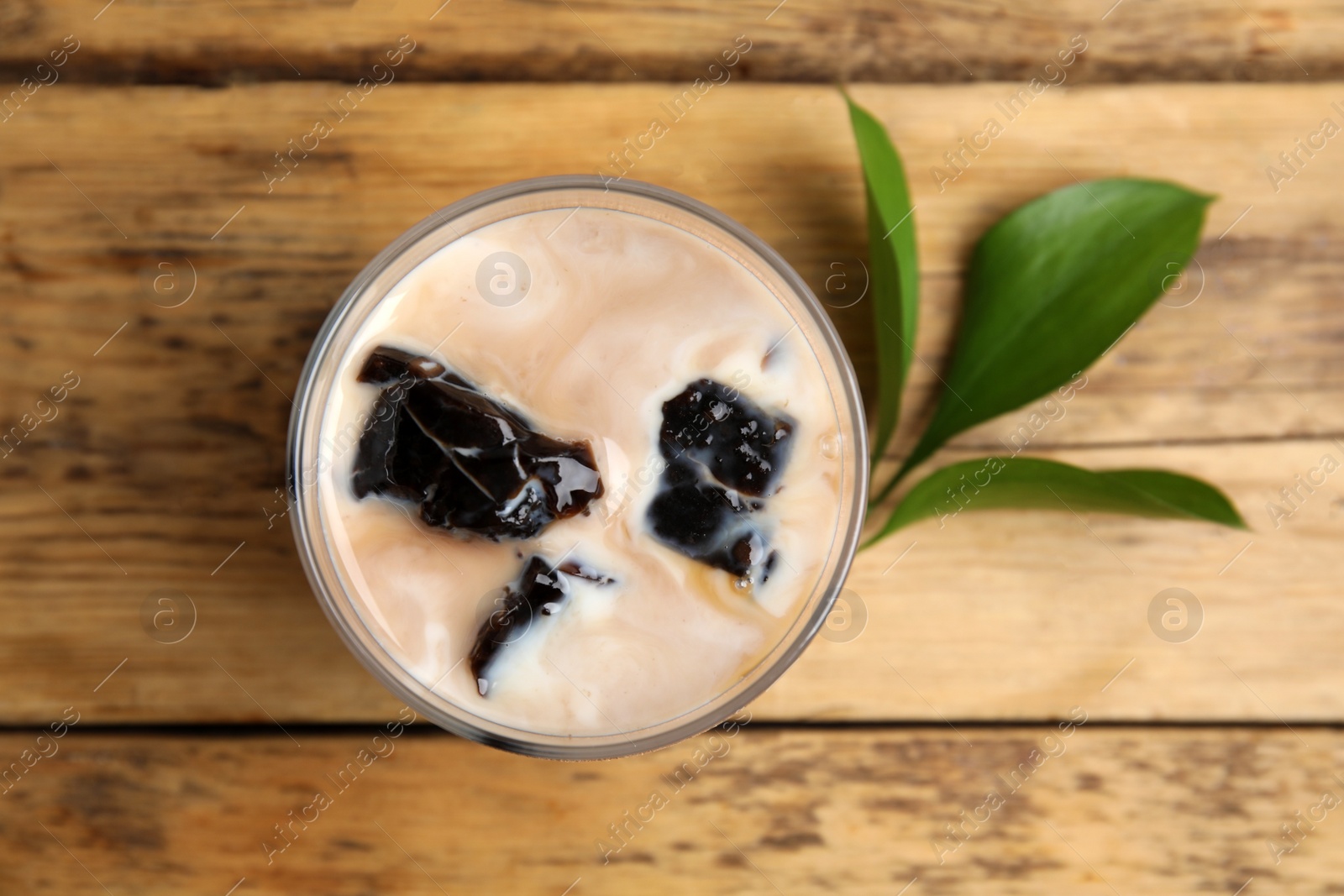 Photo of Glass of milk with grass jelly and green leaves on wooden table, flat lay