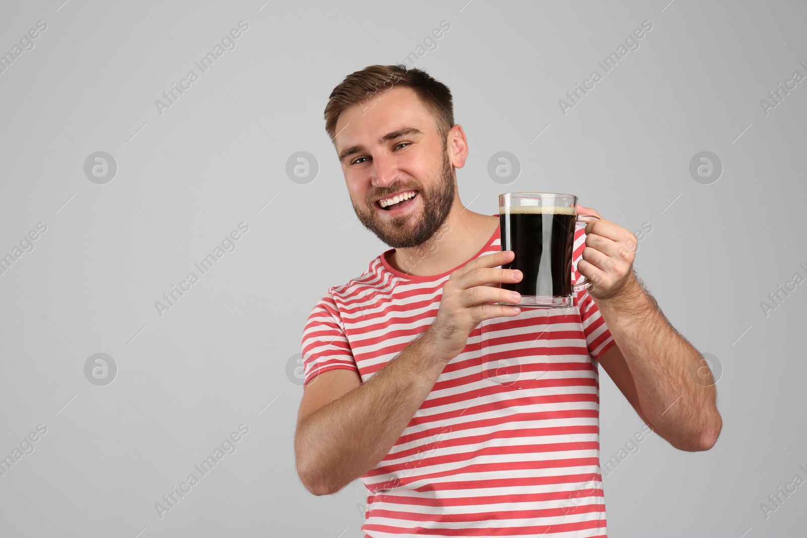 Photo of Handsome man with cold kvass on light grey background. Traditional Russian summer drink