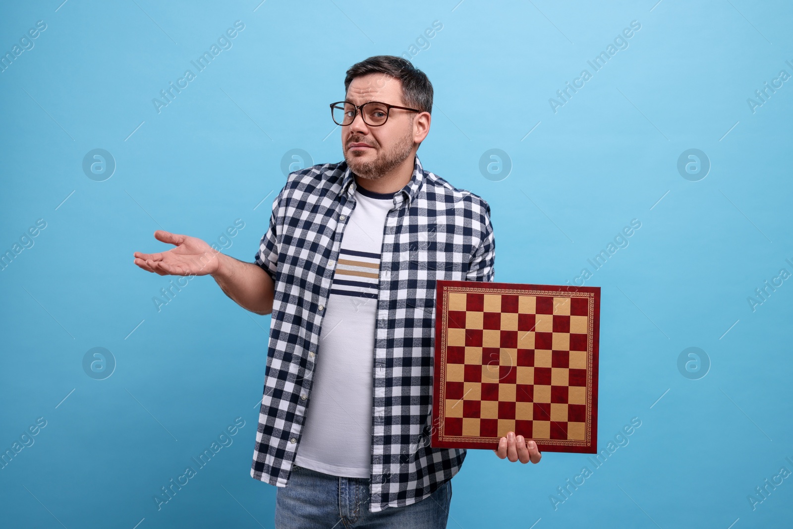 Photo of Puzzled man holding chessboard on light blue background