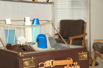 Photo of Vintage suitcase with deodorants and clothes at home, closeup view