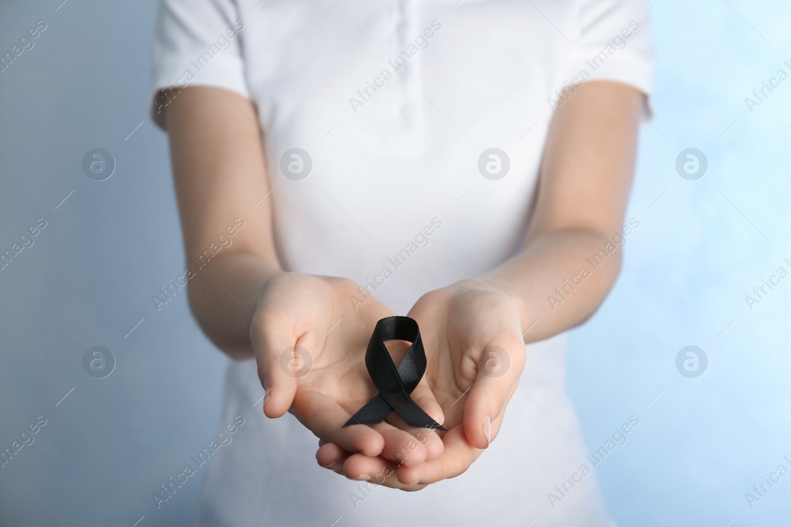 Photo of Woman holding black ribbon on light background, closeup. Funeral symbol