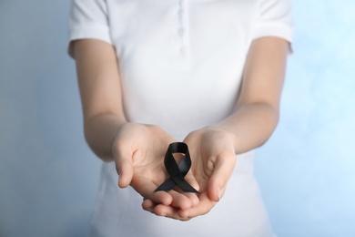 Photo of Woman holding black ribbon on light background, closeup. Funeral symbol