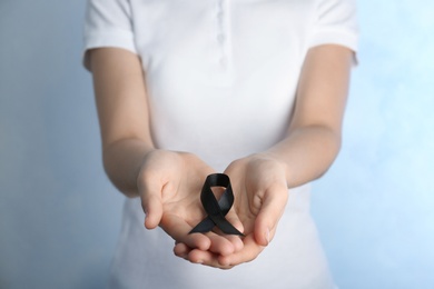 Woman holding black ribbon on light background, closeup. Funeral symbol