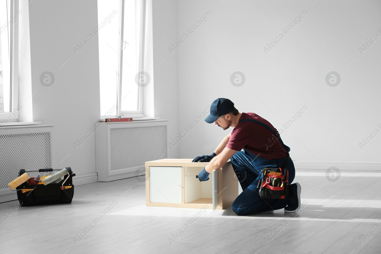 Photo of Handyman in uniform assembling furniture indoors. Professional construction tools