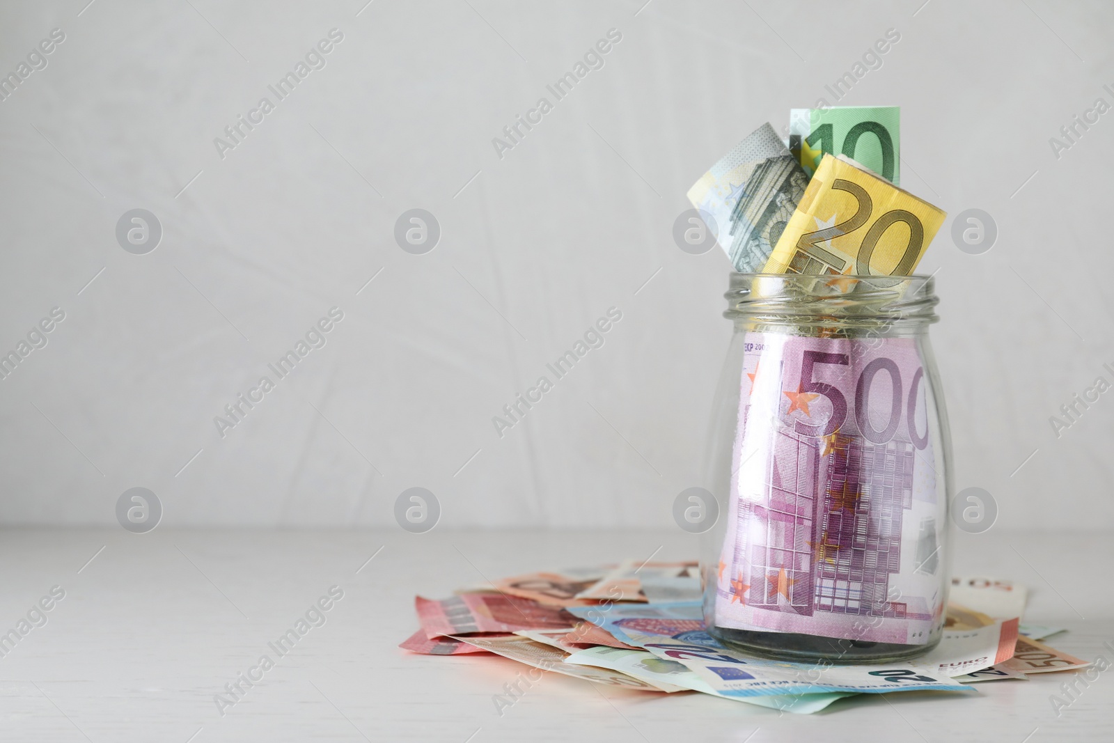 Image of Glass jar full of money on light table. Space for text 