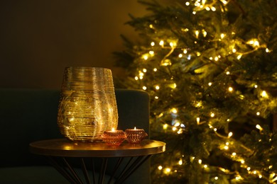 Beautiful Christmas tree with golden lights, vase and scented candles on table indoors