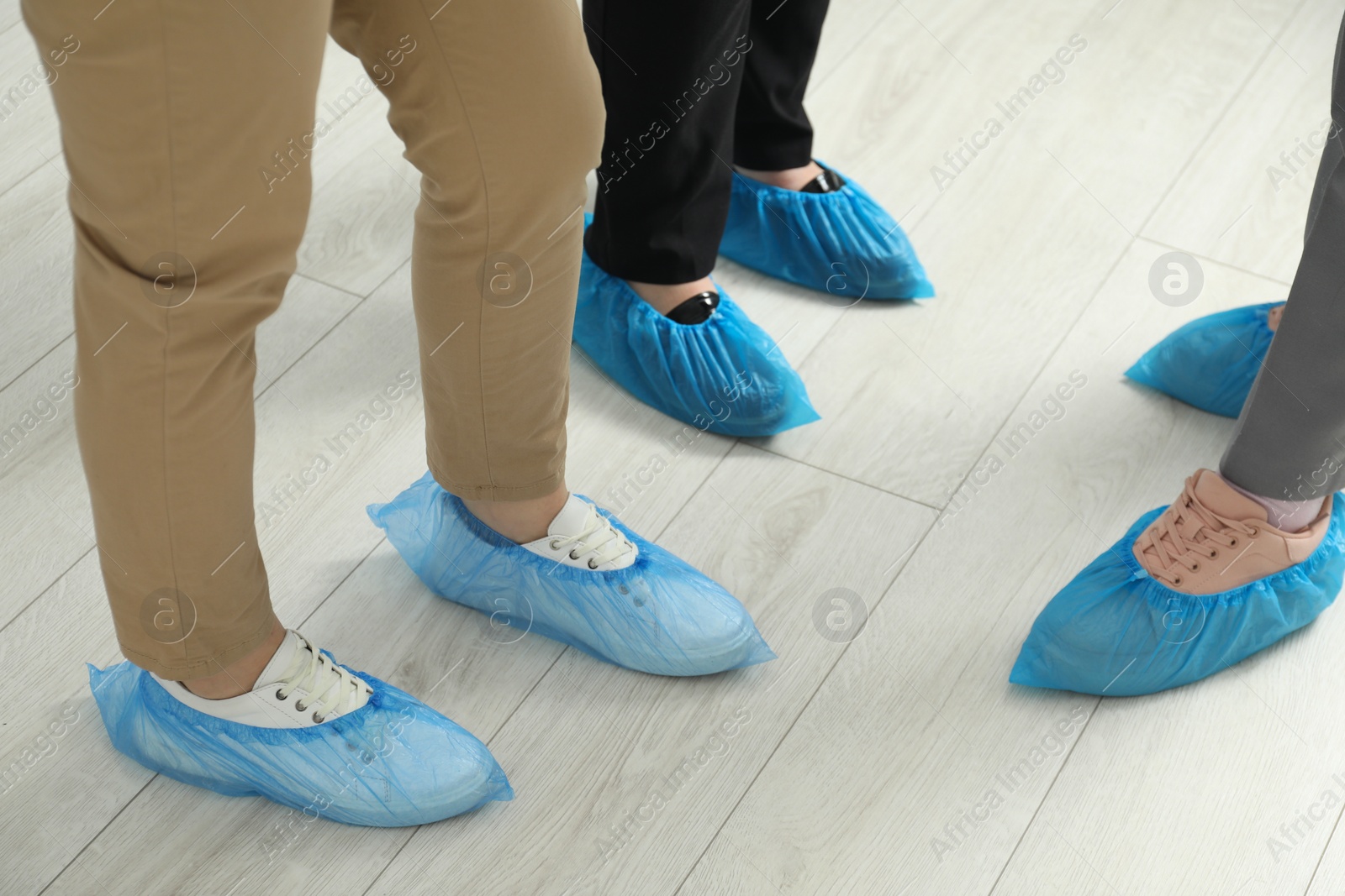 Photo of Women wearing blue shoe covers onto different footwear indoors, closeup