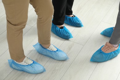 Women wearing blue shoe covers onto different footwear indoors, closeup