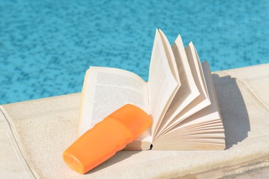 Photo of Open book and sunscreen on swimming pool edge