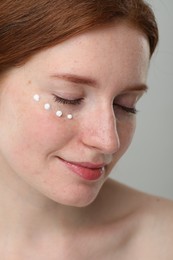 Beautiful woman with freckles and cream on her face against grey background, closeup