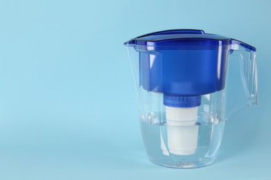 Photo of Filter jug with purified water on light blue background. Space for text
