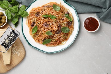 Photo of Delicious pasta with anchovies, tomato sauce, cheese and basil on light grey table, flat lay. Space for text