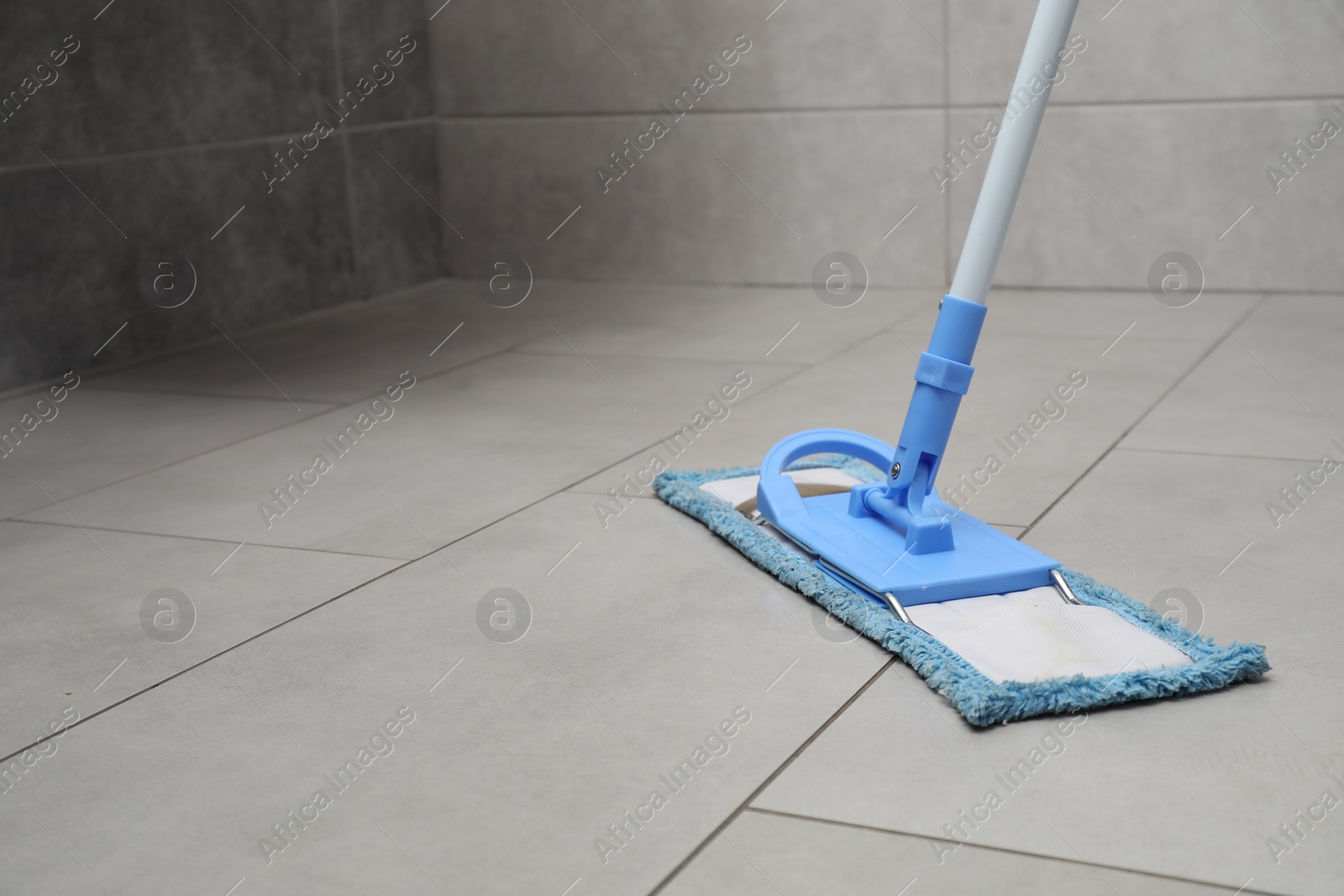 Photo of Cleaning grey tiled floor with mop, space for text