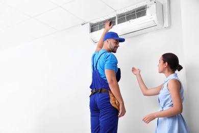 Photo of Professional technician speaking with woman about air conditioner indoors. Space for text