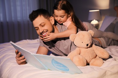 Photo of Father with his daughter reading book in bed at home