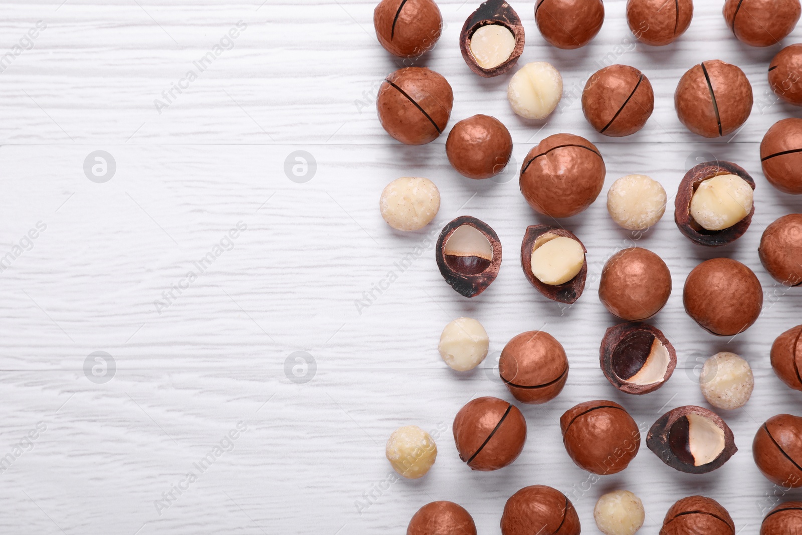 Photo of Delicious Macadamia nuts on white wooden table, flat lay. Space for text