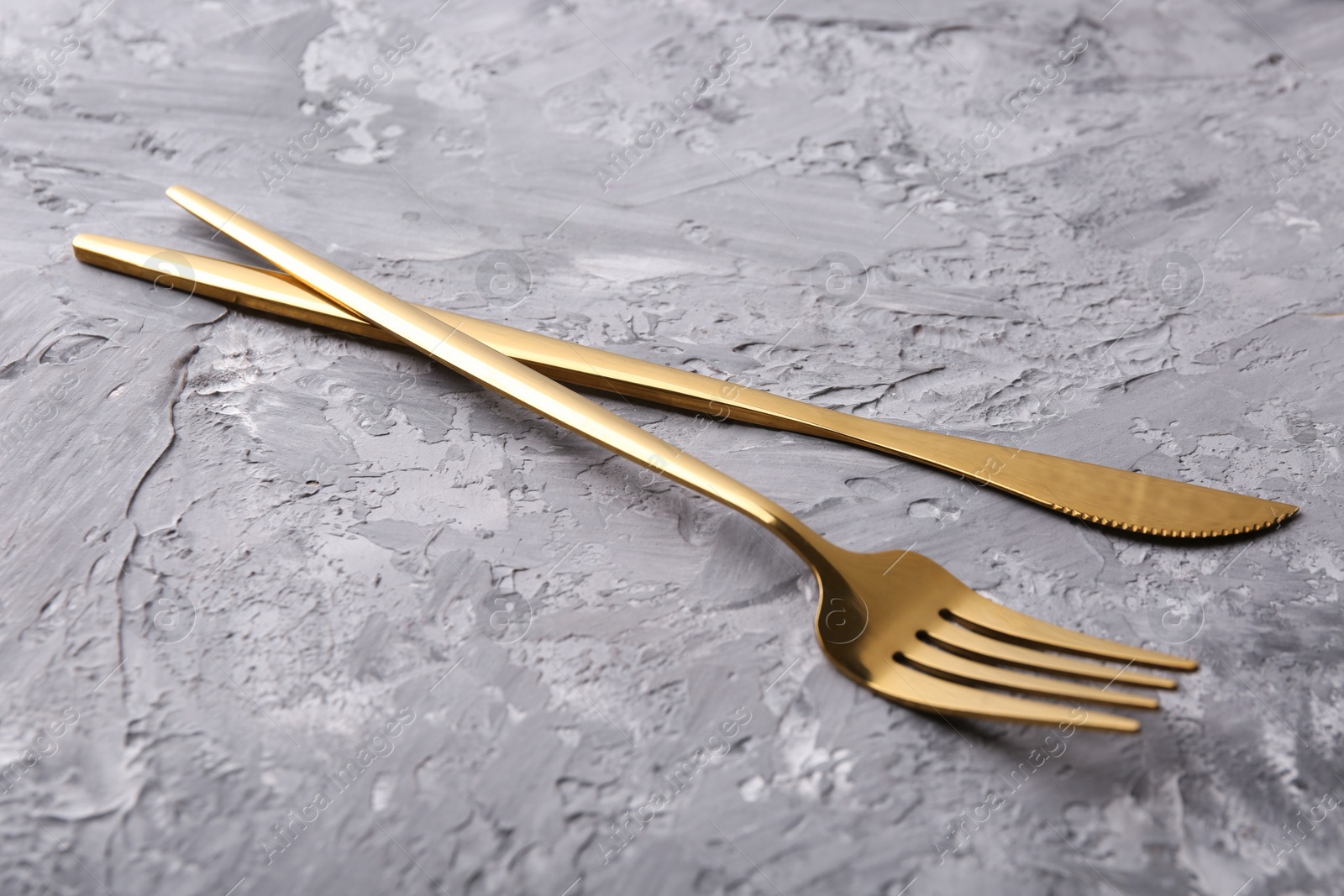 Photo of Stylish cutlery. Golden knife and fork on grey textured table