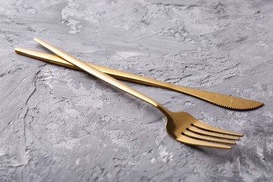 Stylish cutlery. Golden knife and fork on grey textured table