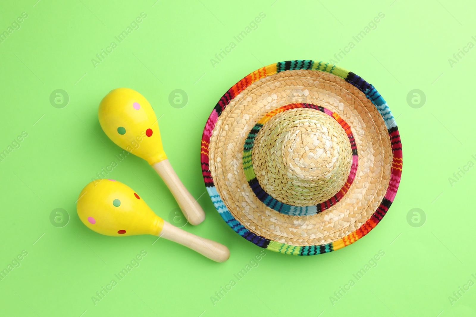 Photo of Mexican sombrero hat and maracas on green background, flat lay