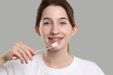 Photo of Smiling woman with dental braces cleaning teeth on grey background