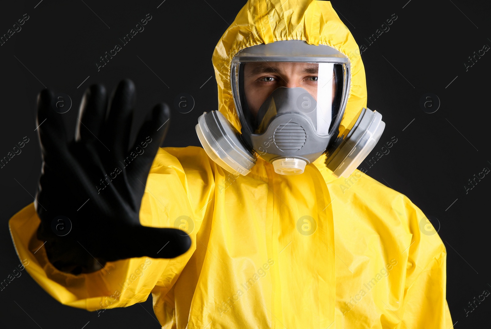 Photo of Man in chemical protective suit making stop gesture on black background. Virus research