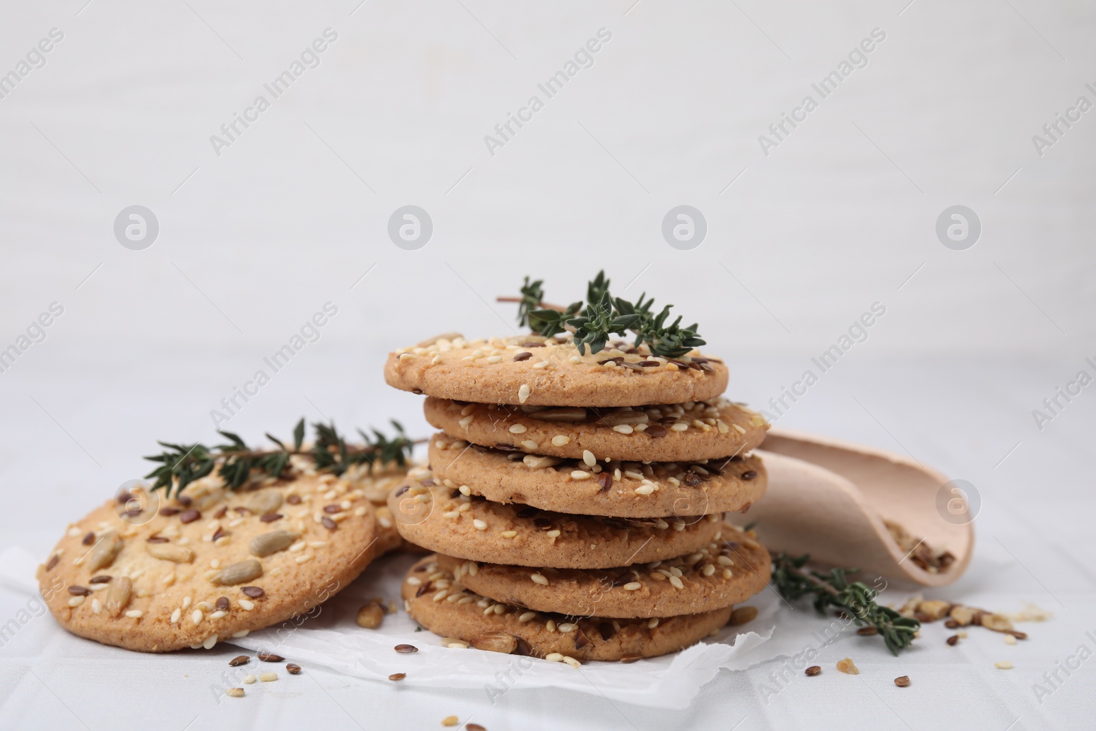 Photo of Cereal crackers with flax, sesame seeds and thyme on white tiled table, closeup