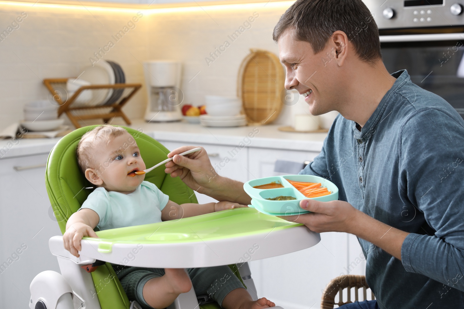 Photo of Father feeding his cute little baby in kitchen