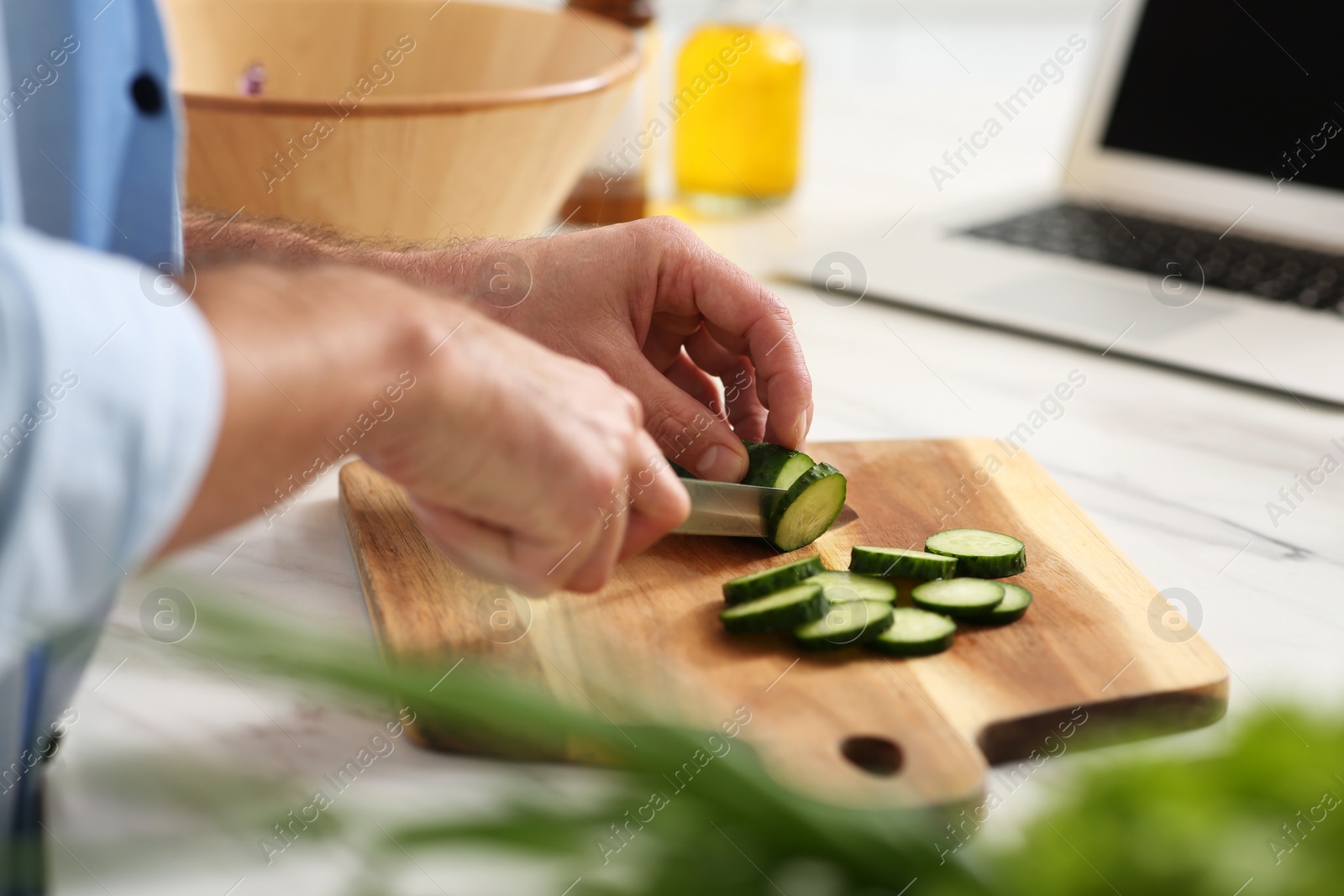 Photo of Man cutting cucumber at table in kitchen, closeup. Online cooking course