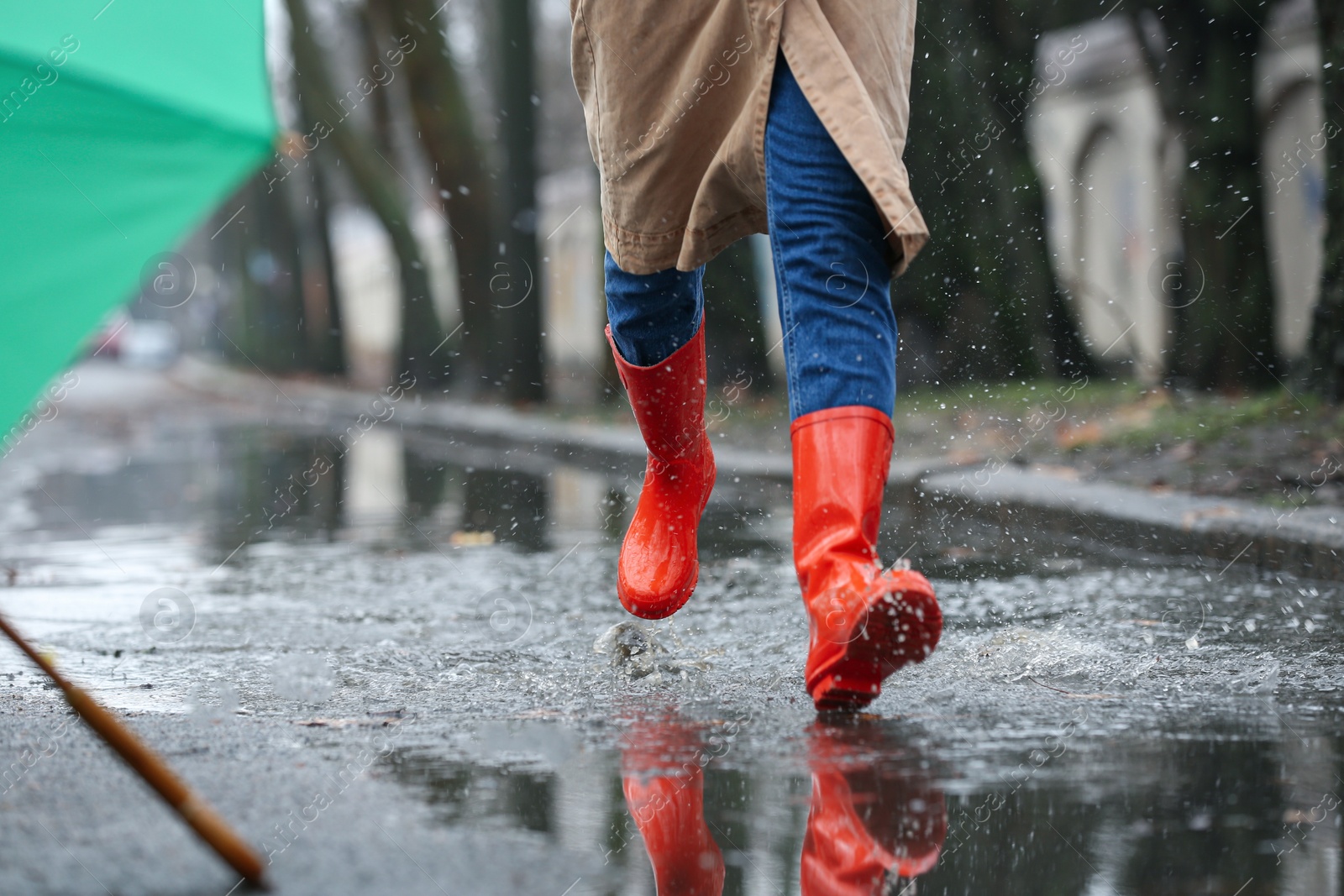 Photo of Woman in rubber boots running after umbrella outdoors on rainy day, closeup