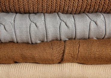 Stack of folded knitted sweaters as background, closeup