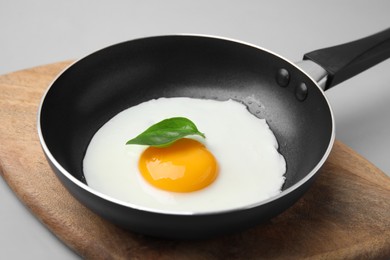 Photo of Pan with tasty fried egg on light grey background, closeup