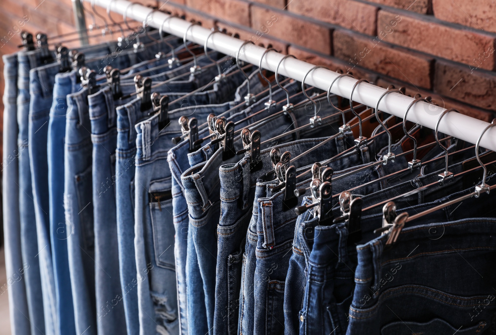 Photo of Rack with stylish jeans near brick wall, closeup