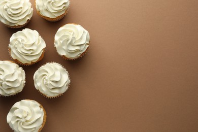 Tasty vanilla cupcakes with cream on dark beige background, top view. Space for text