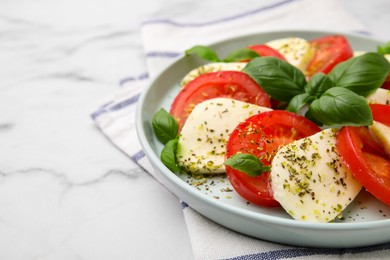 Photo of Caprese salad with tomatoes, mozzarella, basil and spices on white marble table, closeup. Space for text