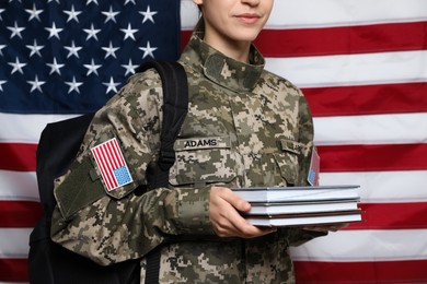 Photo of Female cadet with backpack and books against American flag, closeup. Military education