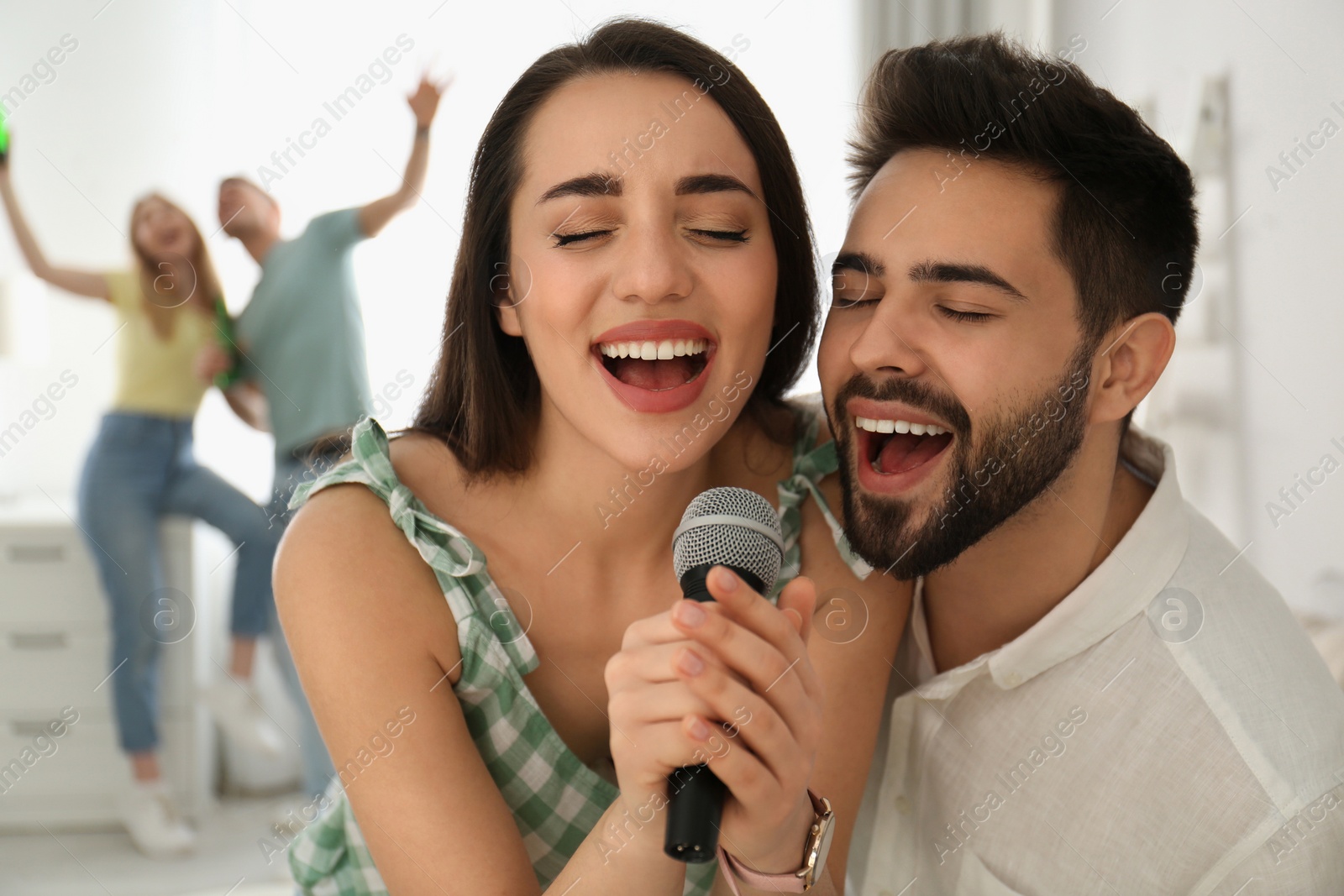 Photo of Happy couple singing karaoke with friends at home