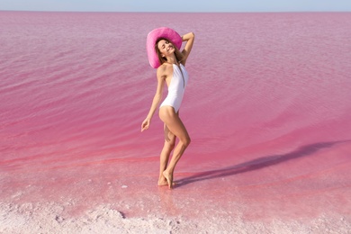 Beautiful woman in swimsuit posing near pink lake on sunny day